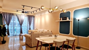A modern living room with a sofa, dining table, chairs, a ceiling fan, and a large window with curtains. - Amerin Residence Mall Apartments (Seri Kembangan)