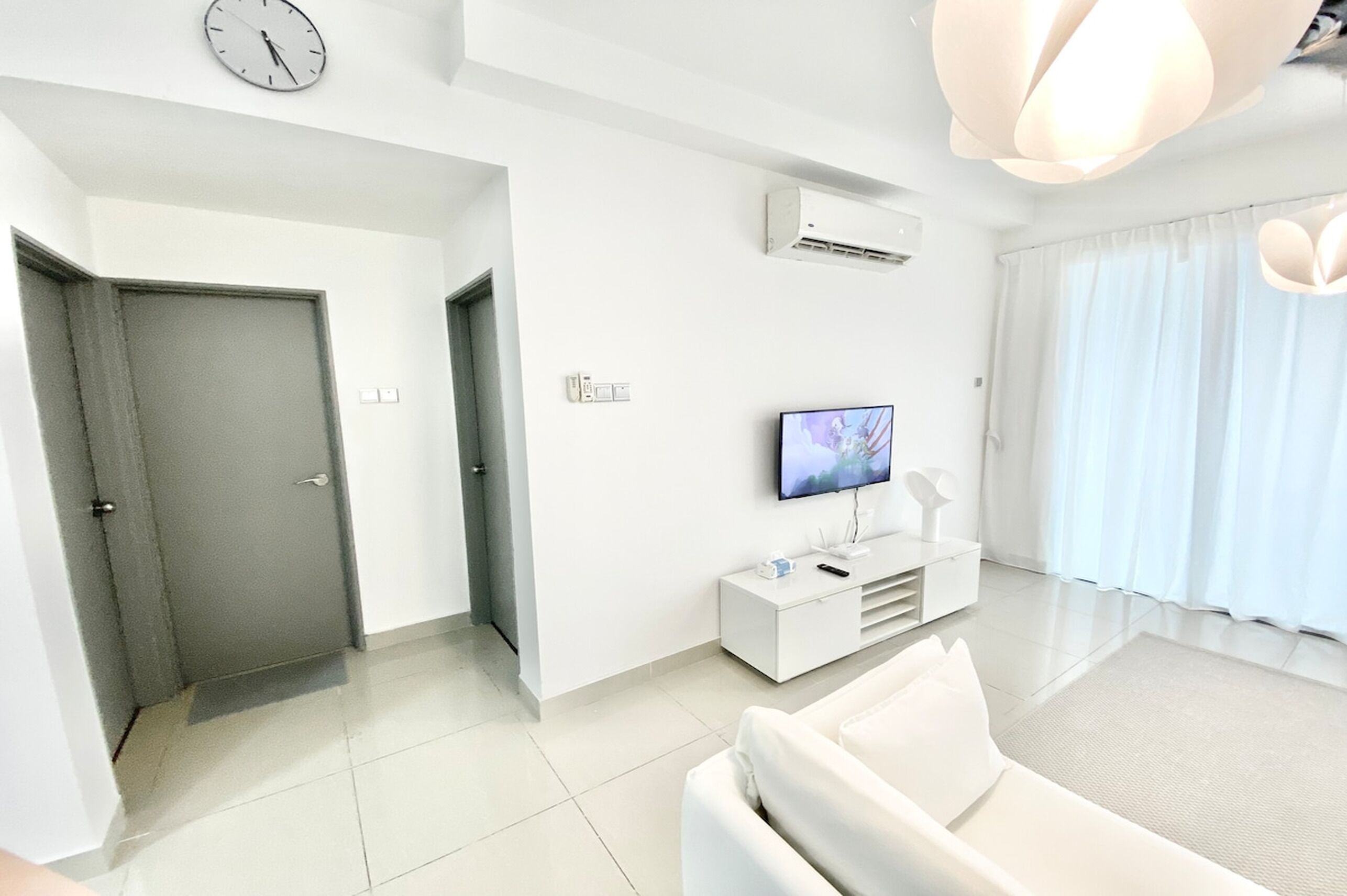 A modern living room with a white sofa, a flat-screen TV, and a minimalist design.