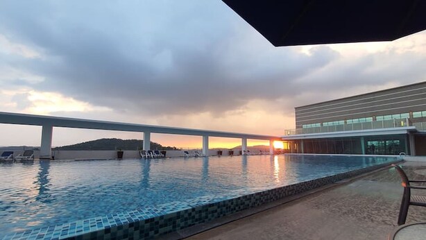A rooftop pool with a view of the sunset and a modern building in the background. - Amerin Residence Mall Apartments (Seri Kembangan)