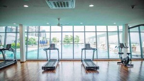 A gym with treadmills and a rowing machine, large windows, and a view of a swimming pool. - Amerin Residence Mall Apartments (Seri Kembangan)