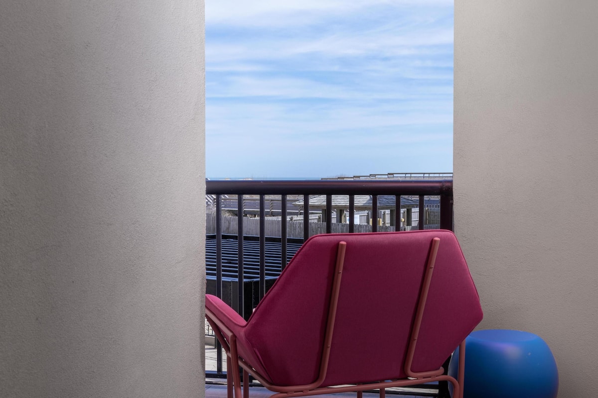A balcony with a view of the sea, a red chair, and a blue exercise ball.