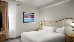 Una camera d'albergo con un letto grande, una televisione a schermo piatto, un quadro appeso e un comodino con una lampada.