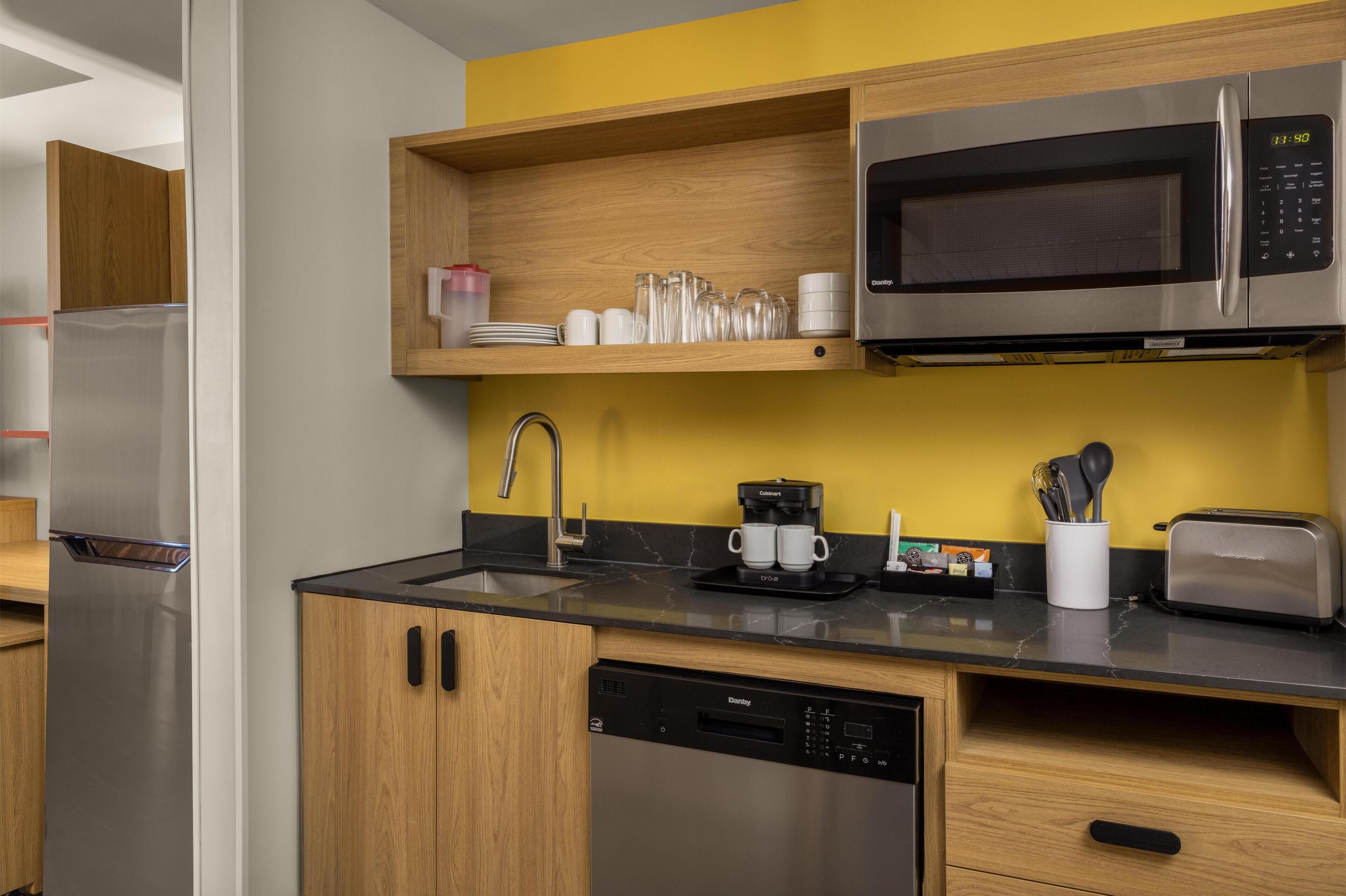 Una cocina moderna con refrigerador de acero inoxidable, microondas, cafetera y lavavajillas.