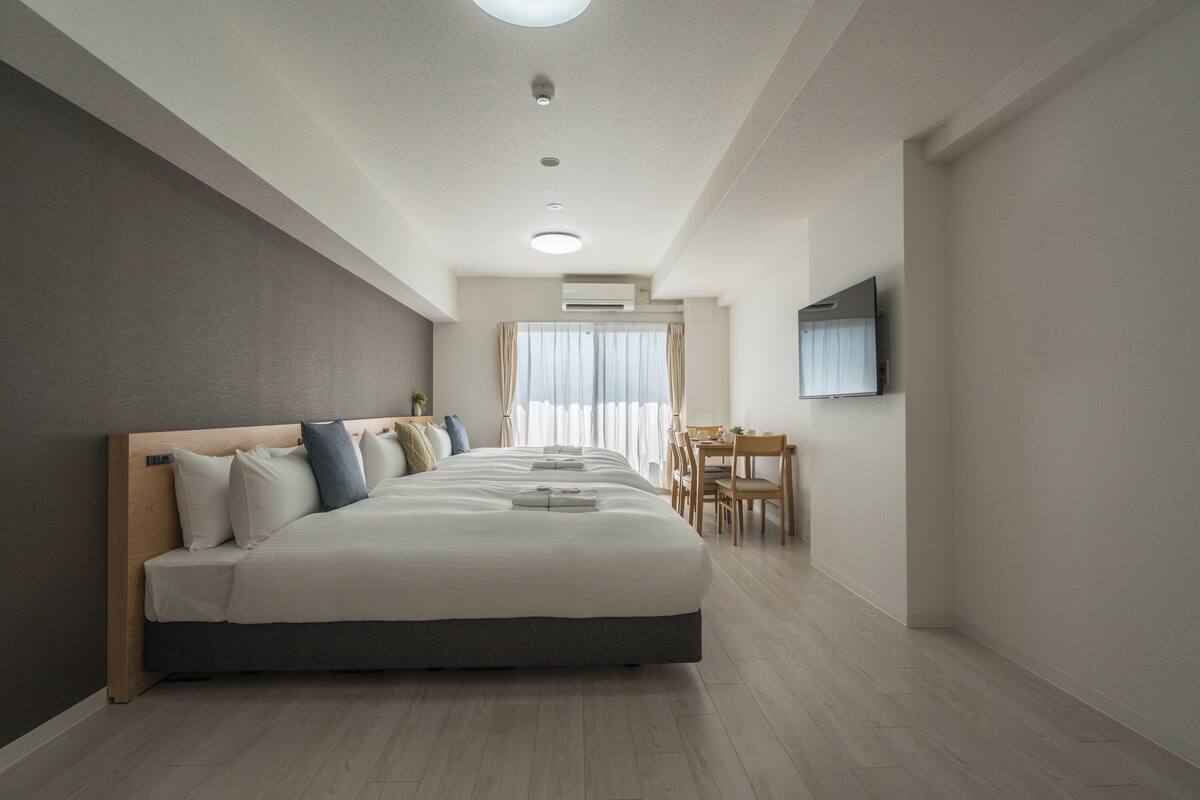Moderni hotellihuone, jossa on suuri sänky, työpöytä ja seinälle asennettu televisio.