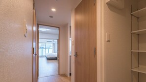 A hallway with a wooden door, a white wall, and a metal shelf unit.