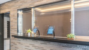A reception area with a modern design, featuring a brick wall, a glass window, and a reception desk with a digital kiosk.