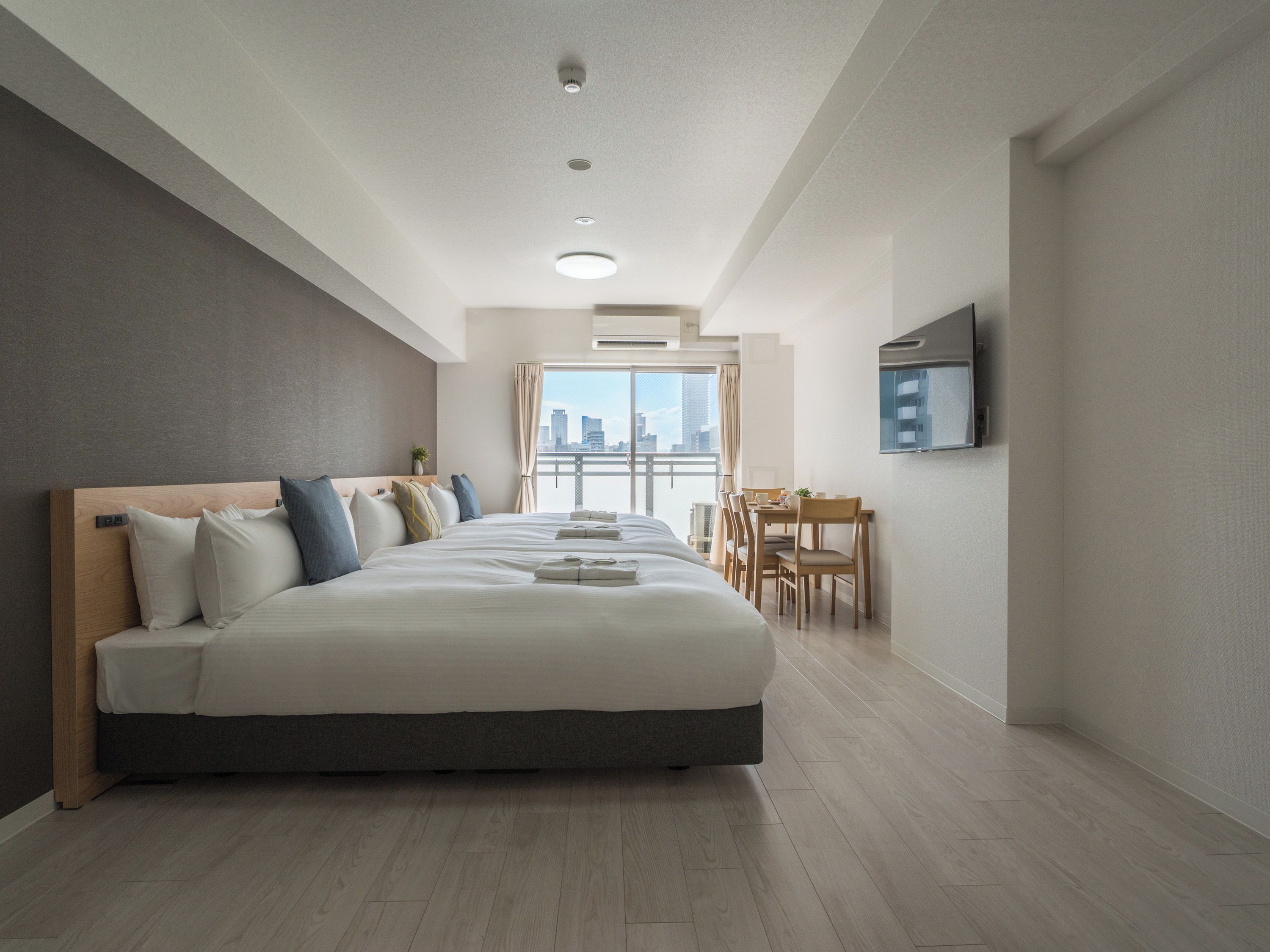 A hotel room with a large bed, a dining area, and a TV on the wall.
