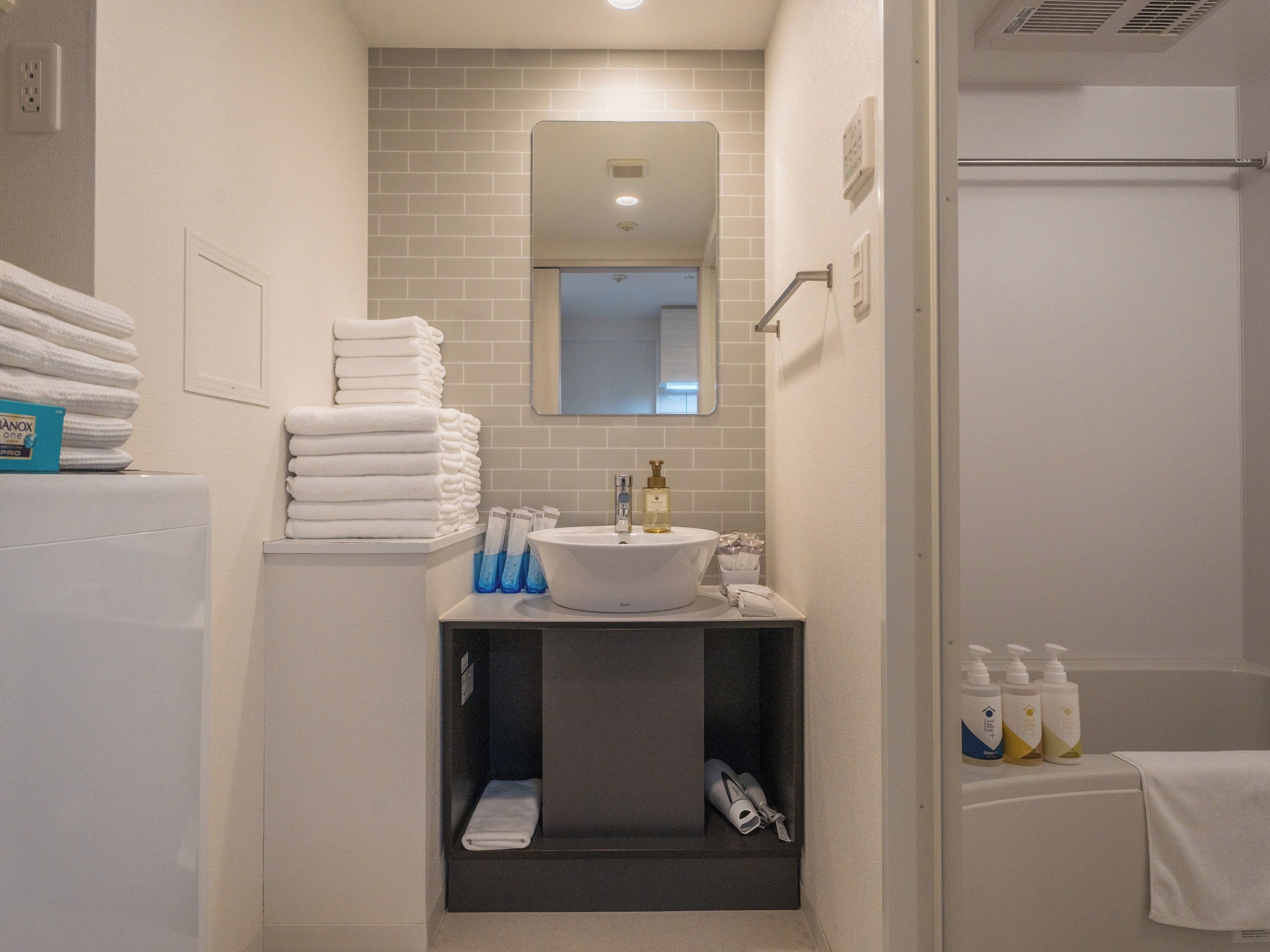 A bathroom with a sink, mirror, and stacked towels.
