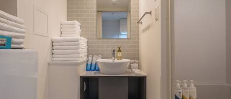 A bathroom with a sink, mirror, and stacked towels.