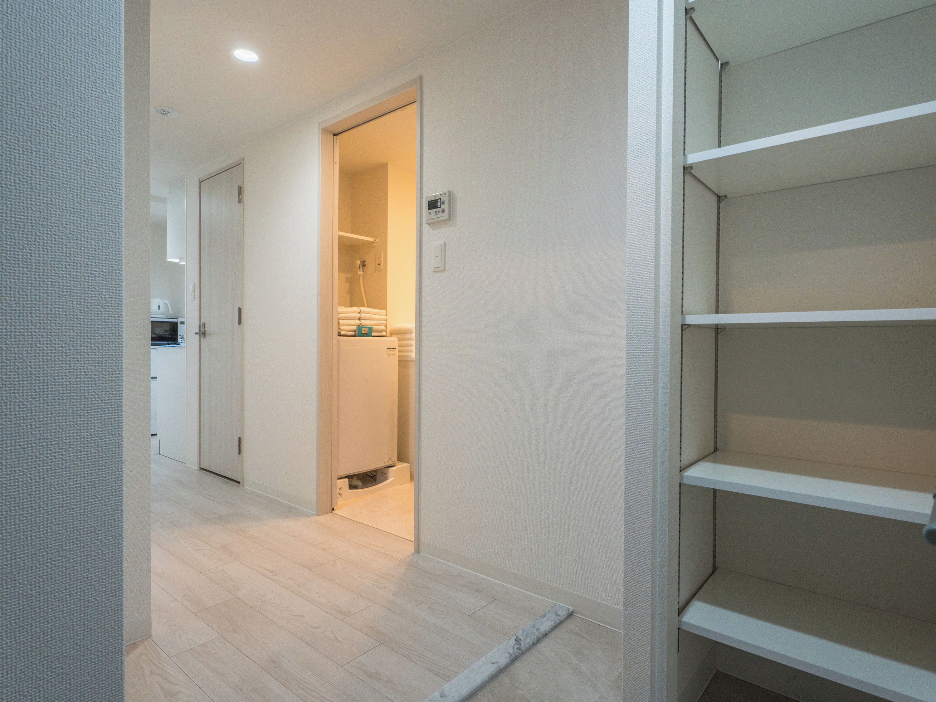 A hallway with a wooden floor, a door leading to a bathroom, and a white shelf unit.