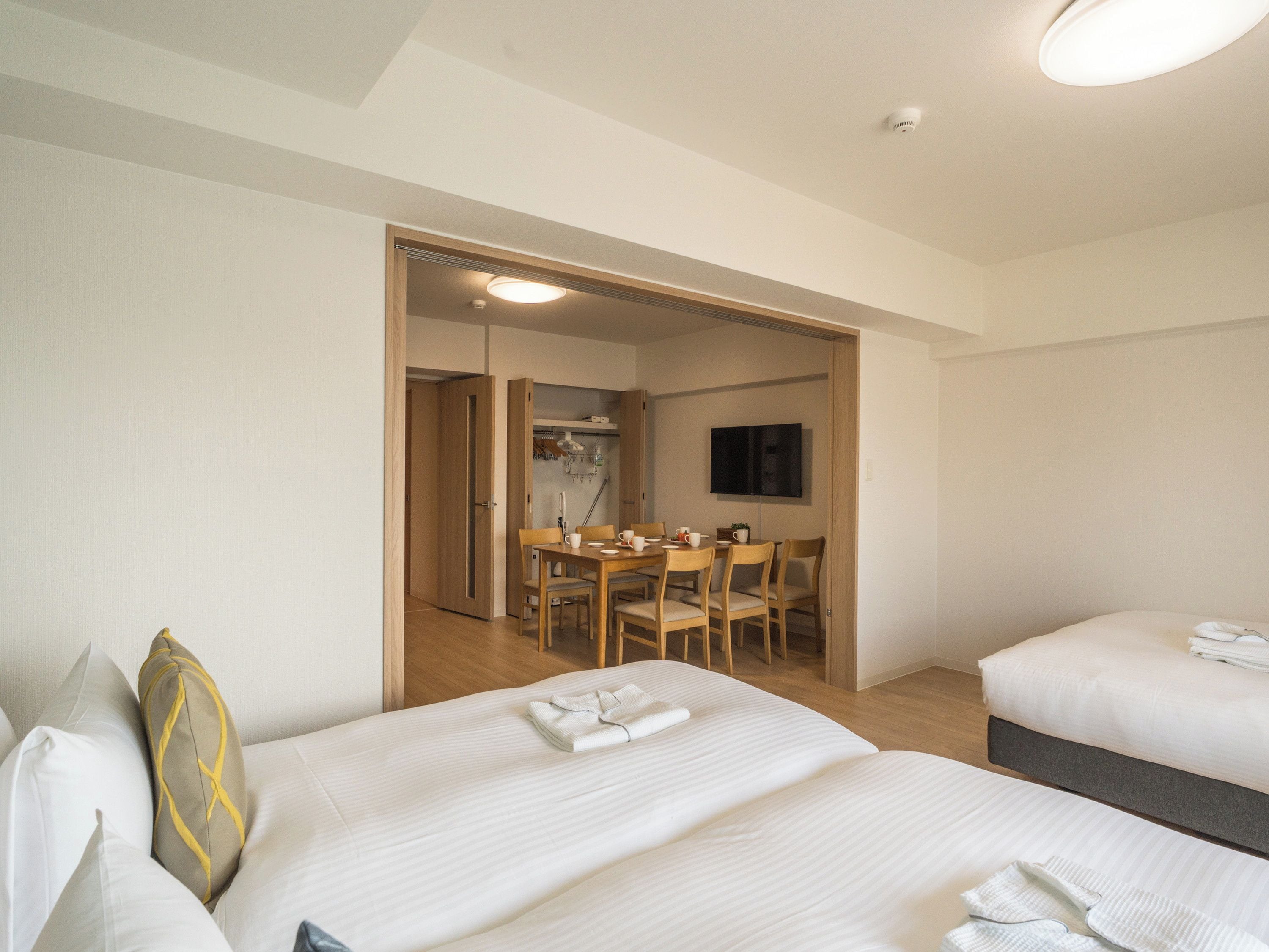 A hotel room with two beds, a dining area with a table and chairs, a TV, and a closet.