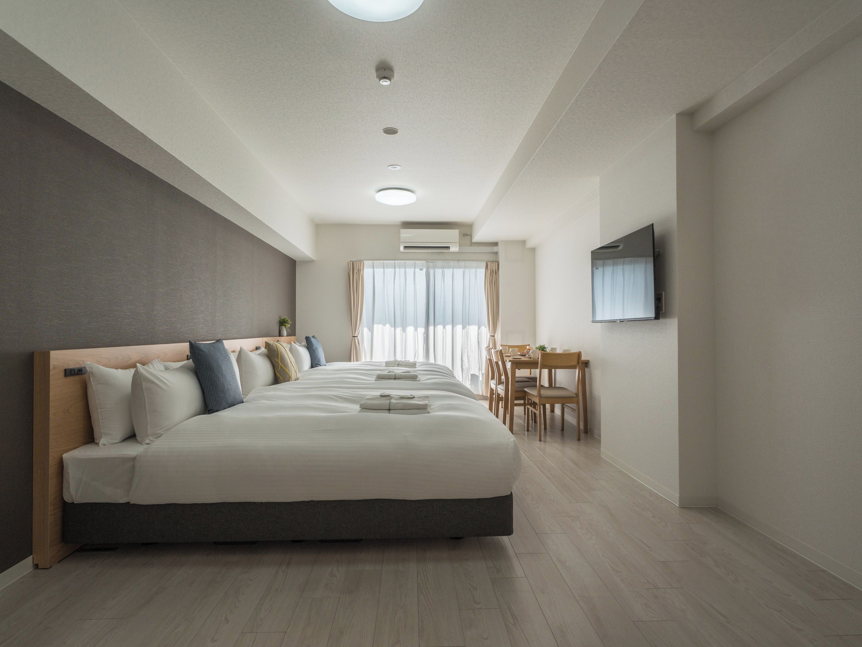 Una habitación de hotel moderna con una cama grande, un rincón de comedor y un televisor montado en la pared.