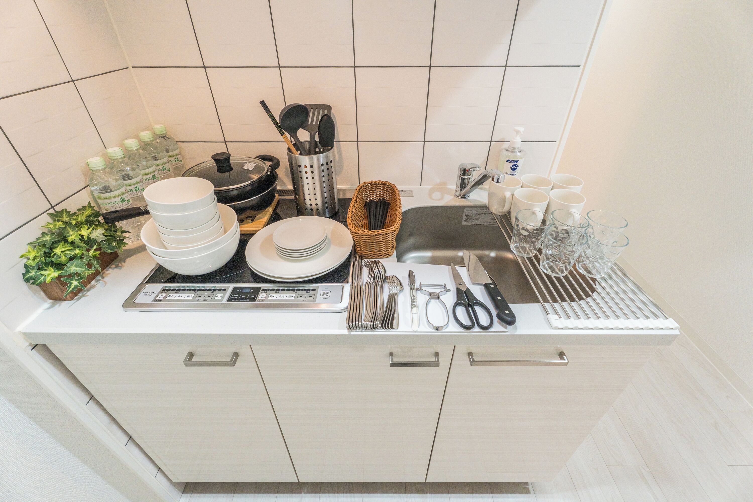 Moderni keittiö, jossa on valkoiset kaapit, ruostumattomasta teräksestä valmistettu työtaso sekä erilaisia keittiövälineitä ja -laitteita.
