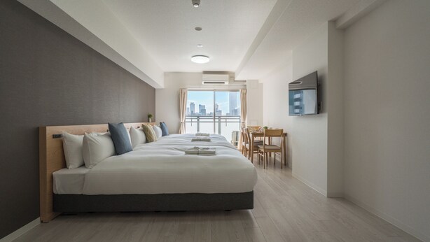 A modern hotel room with a large bed, a dining area, and a city view.