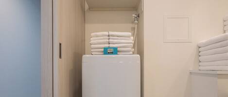 A compact bathroom with a built-in washer and dryer, a shower, and a stack of folded towels.