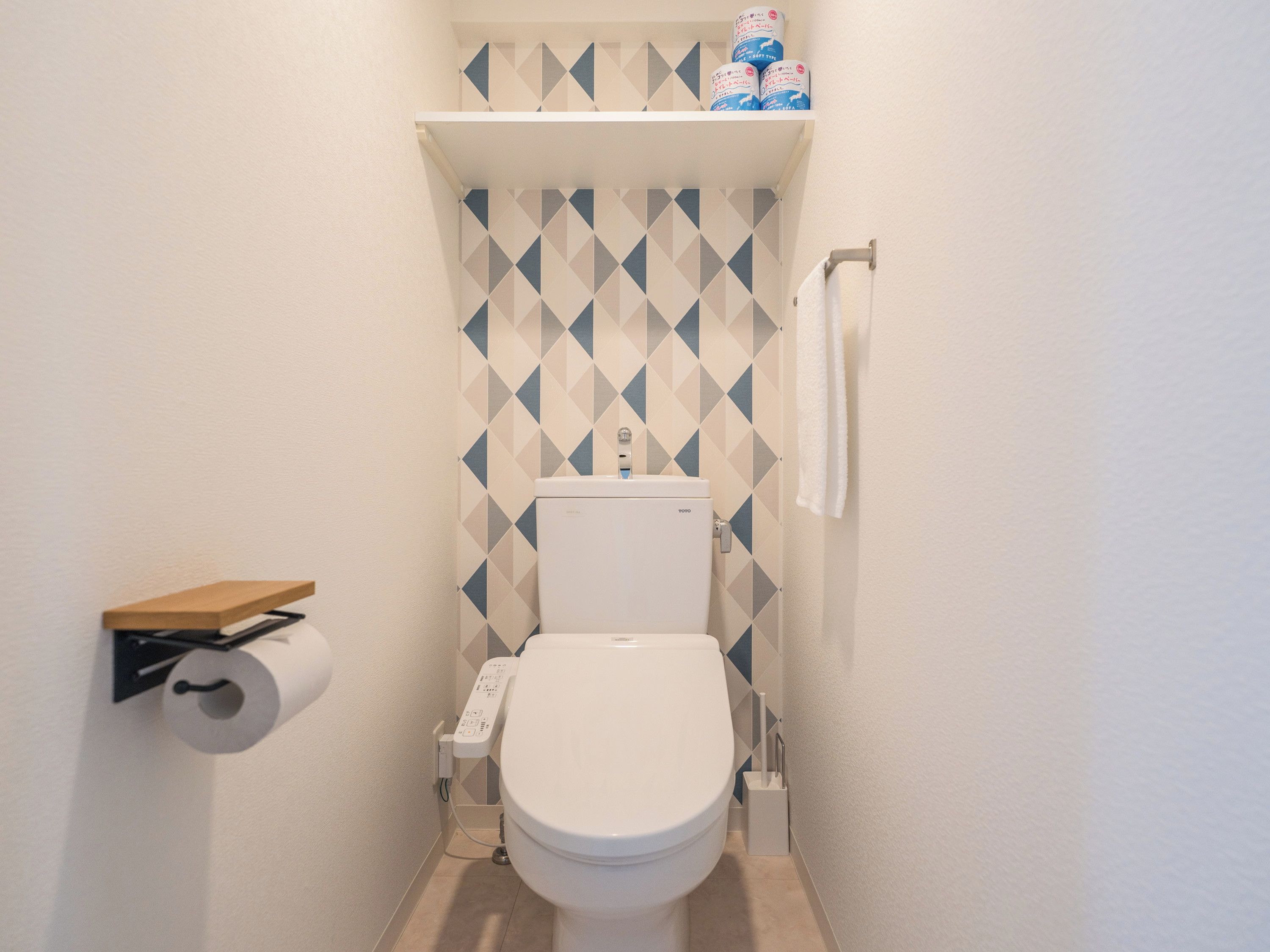 A compact bathroom with a toilet, a roll of toilet paper on a holder, and a shelf above the toilet with toilet paper rolls.