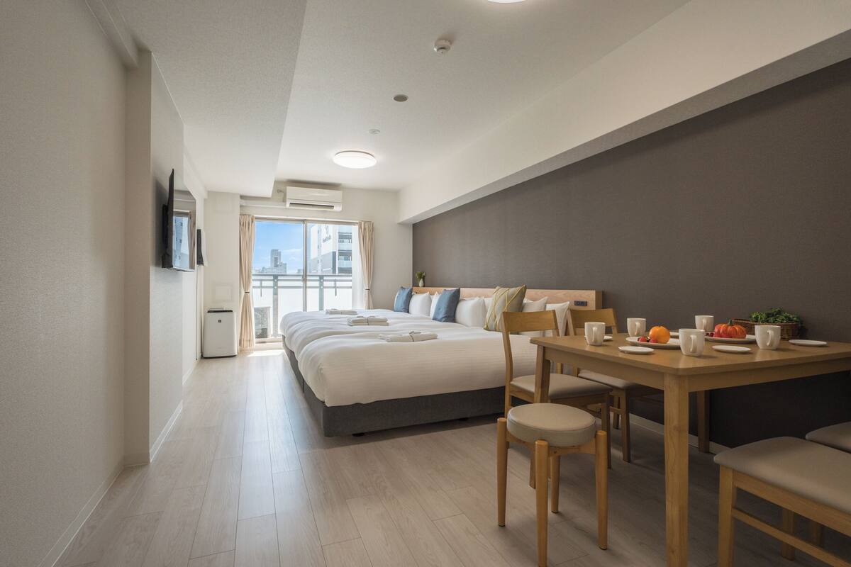 Moderni hotellihuone, jossa on suuri sänky, ruokapöytä tuoleineen ja ikkunasta avautuva näkymä kaupunkiin.