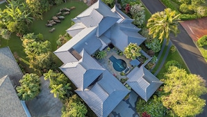 Une vue aérienne d’une maison avec une piscine, entourée d’une végétation luxuriante et de palmiers.