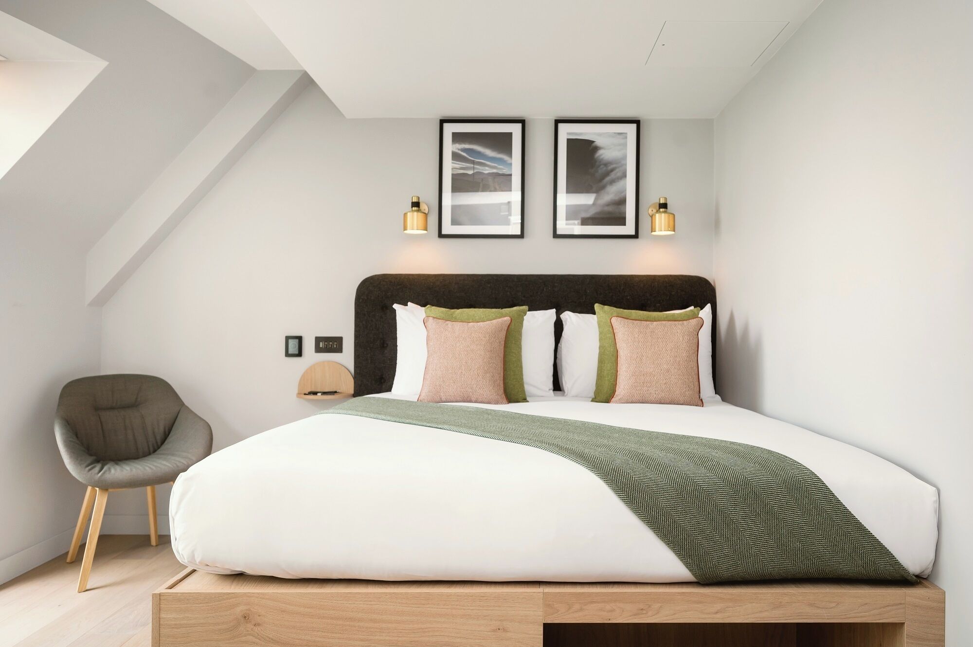 A modern bedroom with a large bed, a chair, and two framed pictures on the wall.