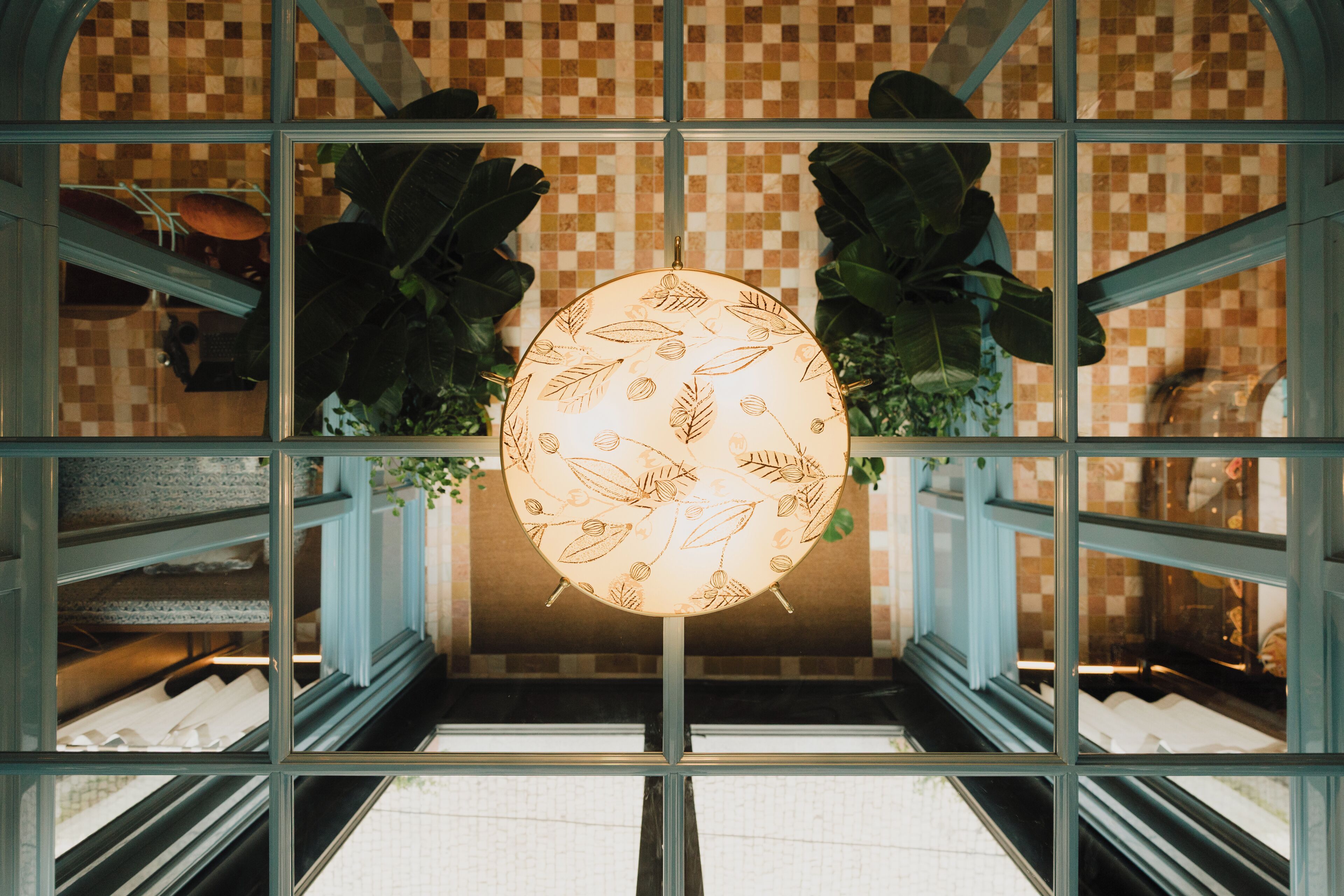 A chandelier with a leaf pattern, a checkered wall, and green plants.