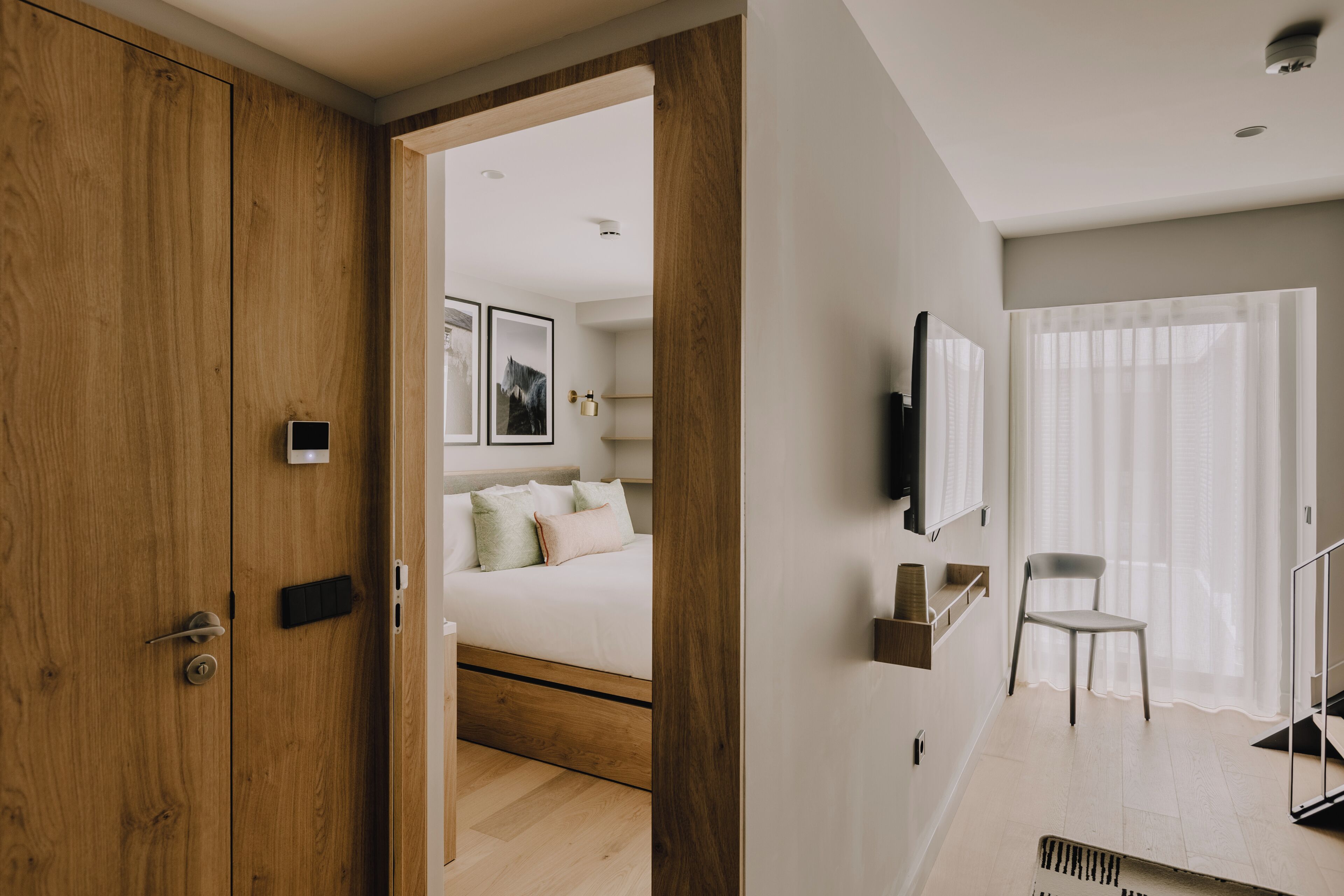 Ein Schlafzimmer mit einem Holzschrank, einem Bett mit Kissen, einem Wand-Fernseher und einem Sessel.