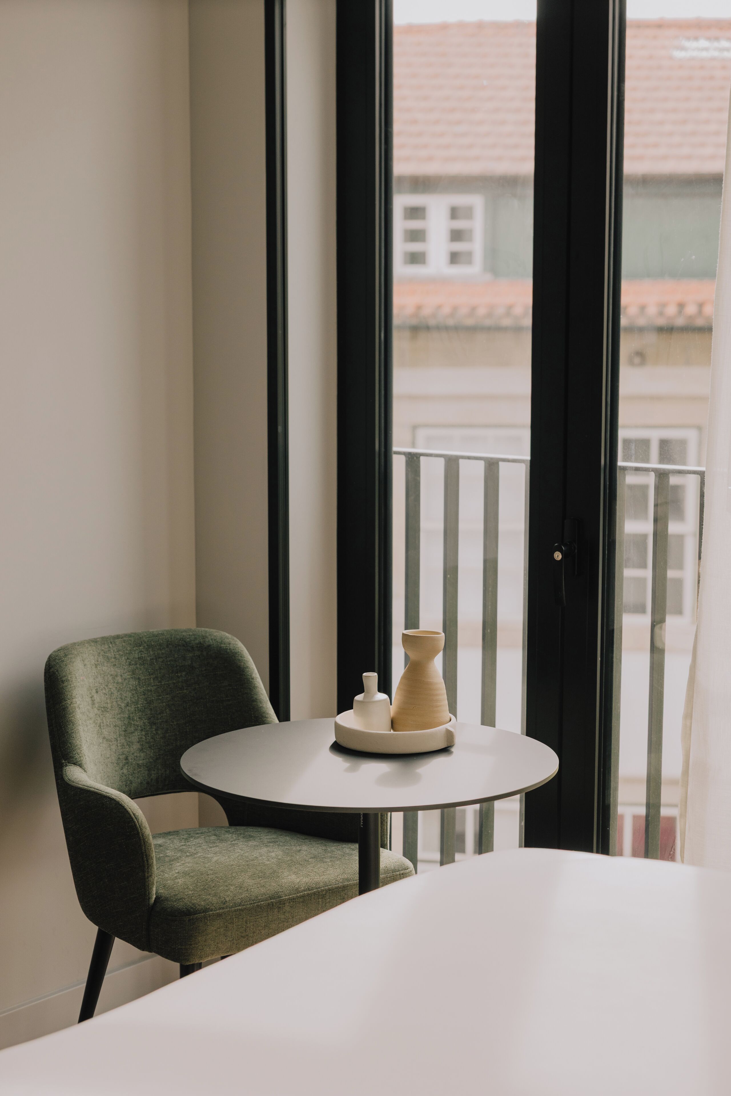 Une pièce avec un fauteuil vert, une petite table ronde et une vue sur un balcon doté d’une balustrade.