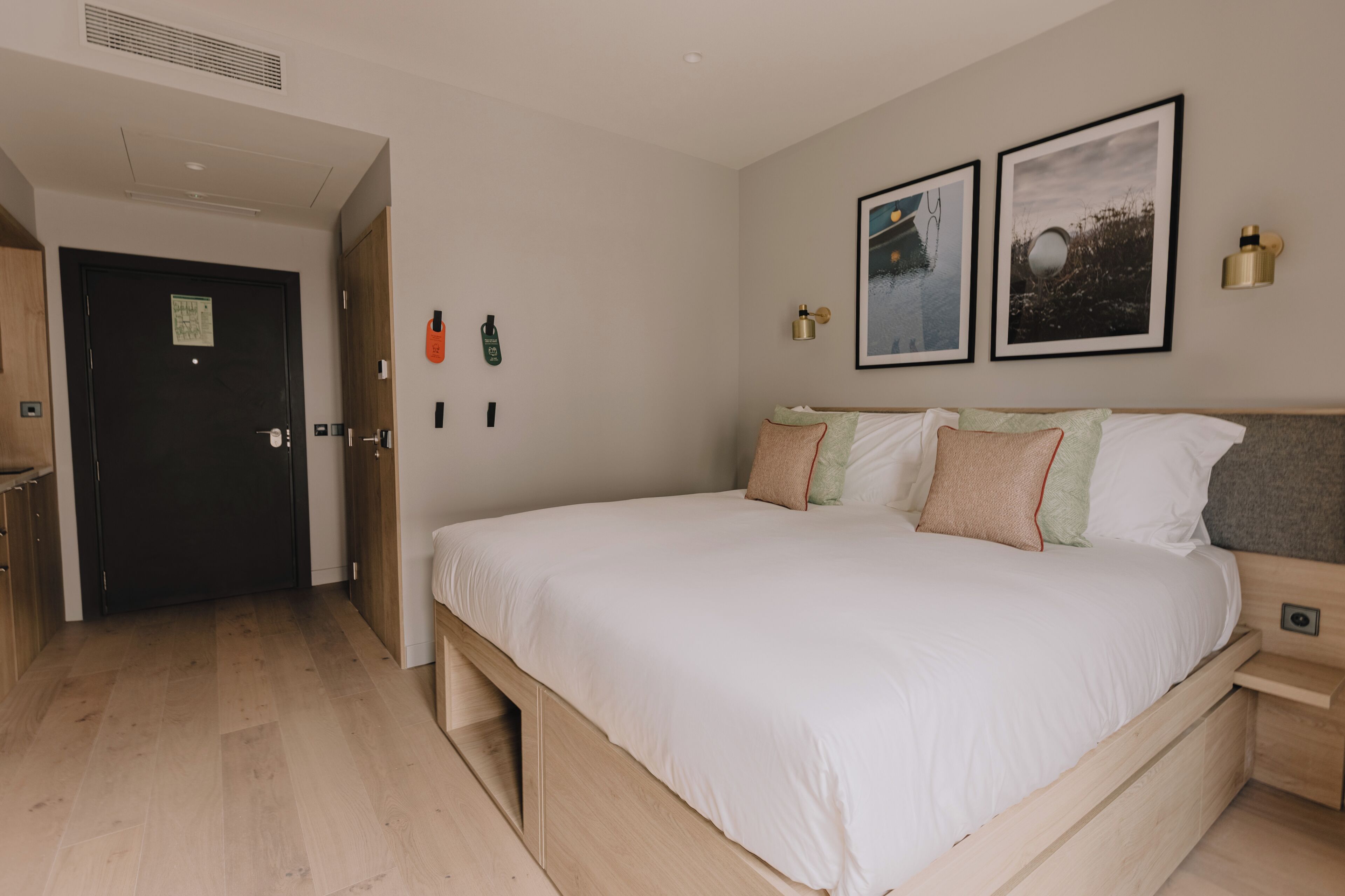 A bedroom with a bed, a door, a wall-mounted light, and two framed pictures.