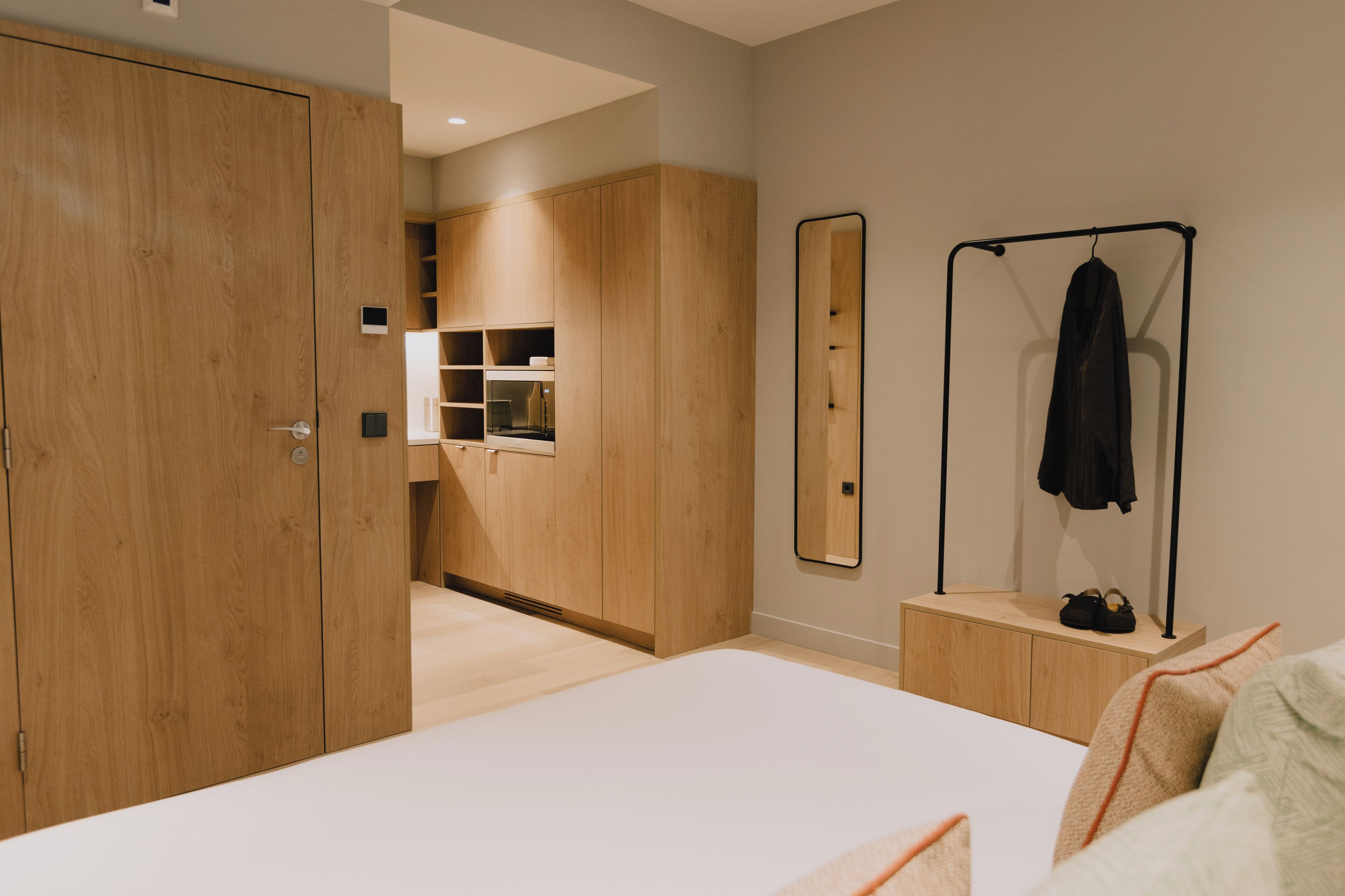 A bedroom with a large bed, wooden wardrobe, built-in shelving, a mirror, and a coat rack.