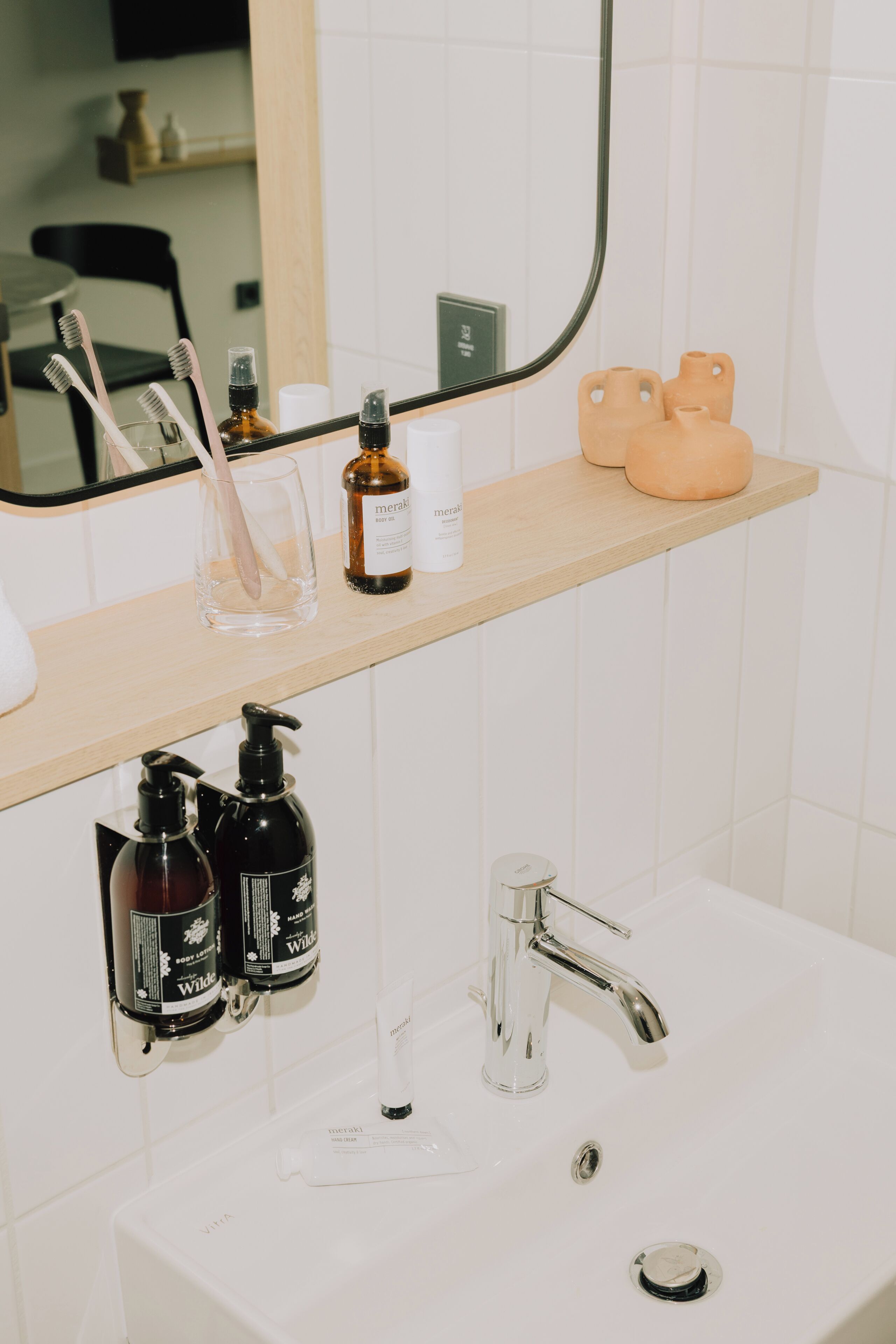 A bathroom with a mirror, toothbrushes, a soap dispenser, and a sink.