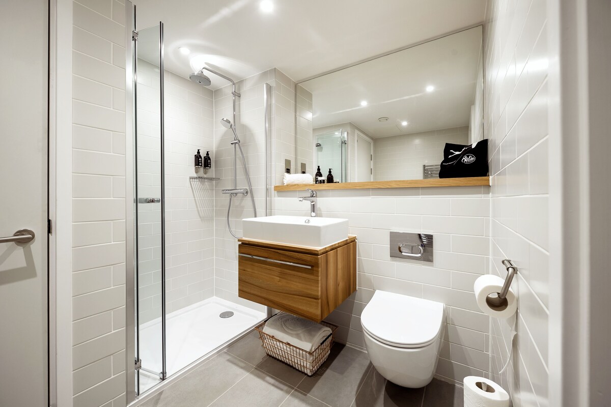 Une salle de bain moderne avec une douche à parois de verre, un meuble-lavabo en bois, des toilettes blanches et un miroir au-dessus du lavabo.