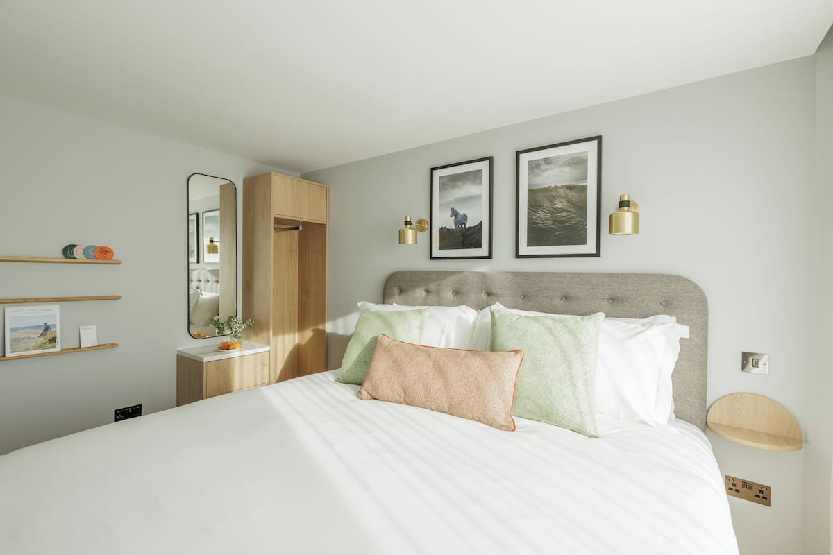 A neatly arranged bedroom with a bed, bedside tables, a mirror, and wall-mounted artwork.