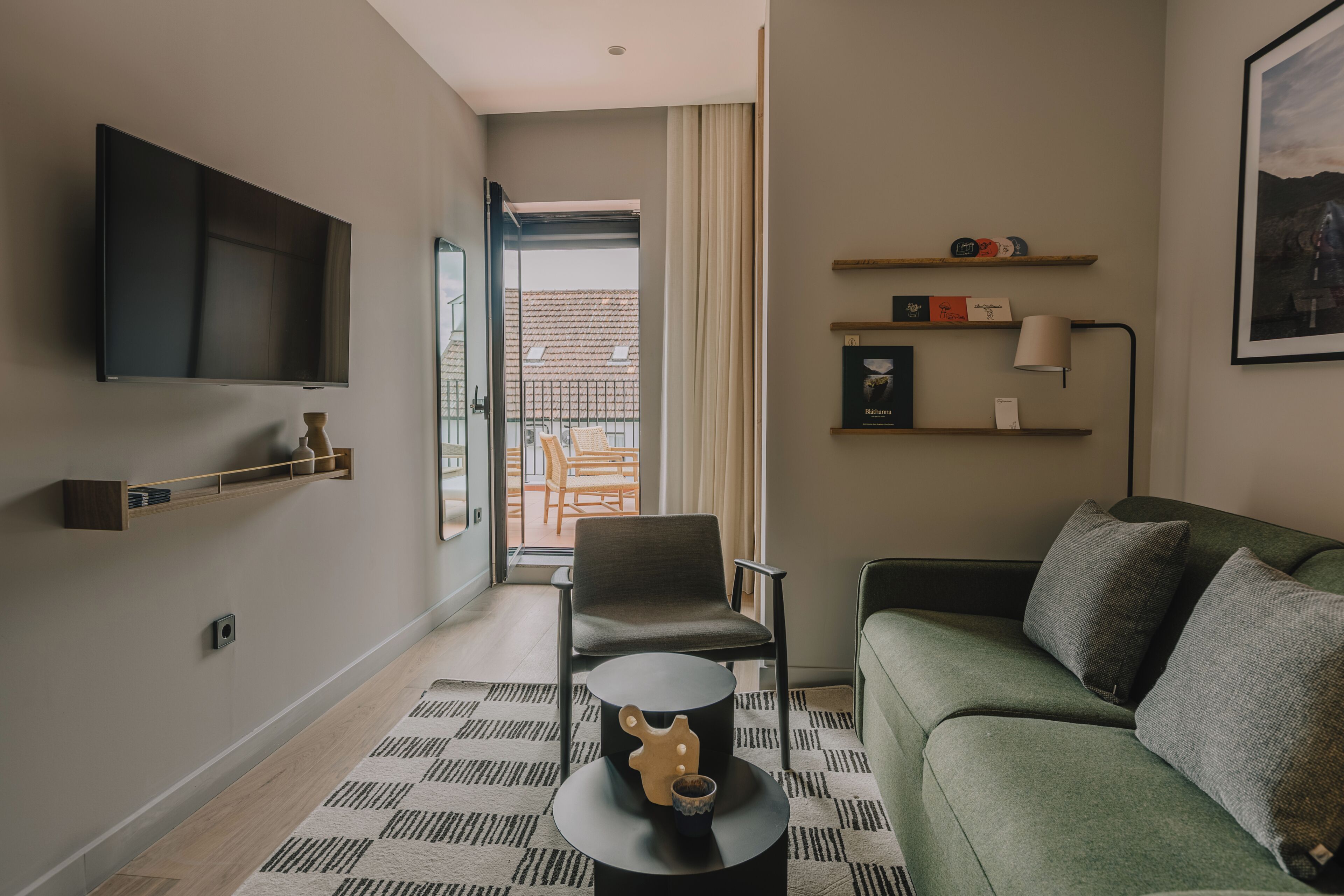 Una sala moderna con televisor de pantalla plana, un sofá, una silla, una mesa de centro y vistas al balcón.