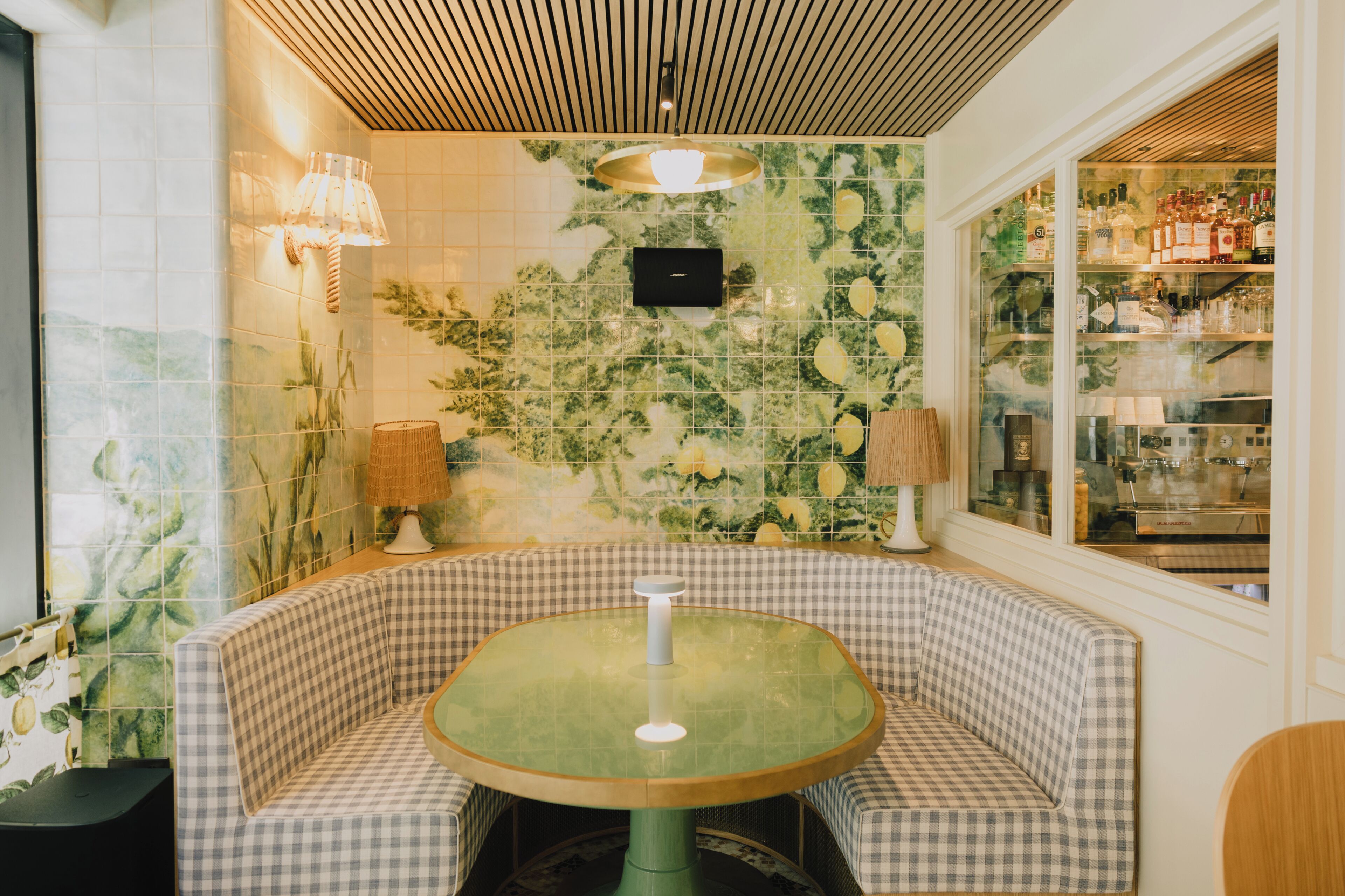 Un sofá y una mesa a cuadros en una habitación con un mural de azulejos, techo de madera y una ventana con estanterías.