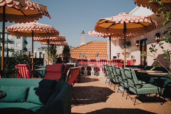 An outdoor seating area with tables and chairs, umbrellas, and a building with a tiled roof in the background. - Wilde Aparthotels Porto, Clérigos (Porto)