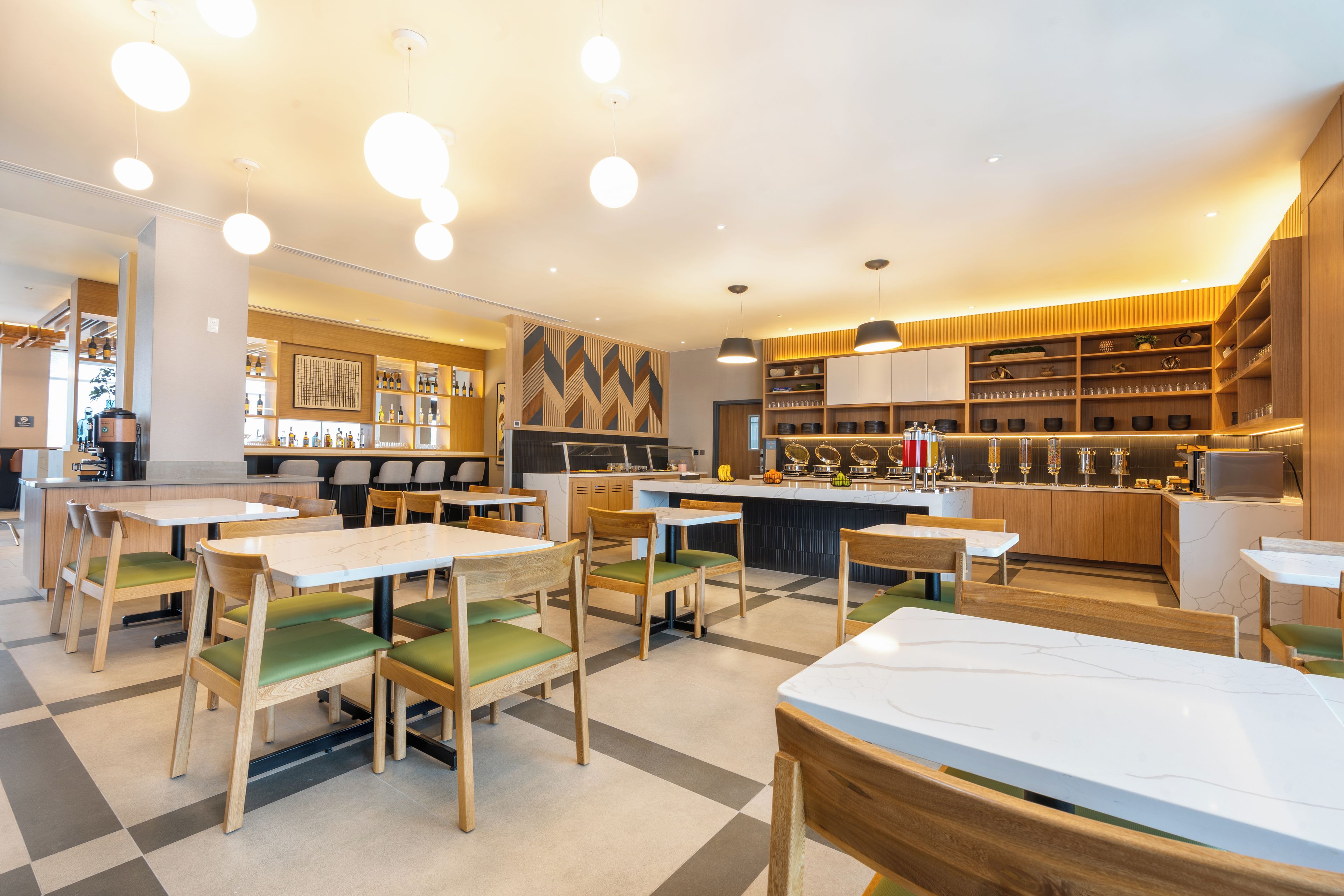 Un interior de restaurante moderno con mesas y sillas de madera, una zona de bar y diverso equipo de cocina.