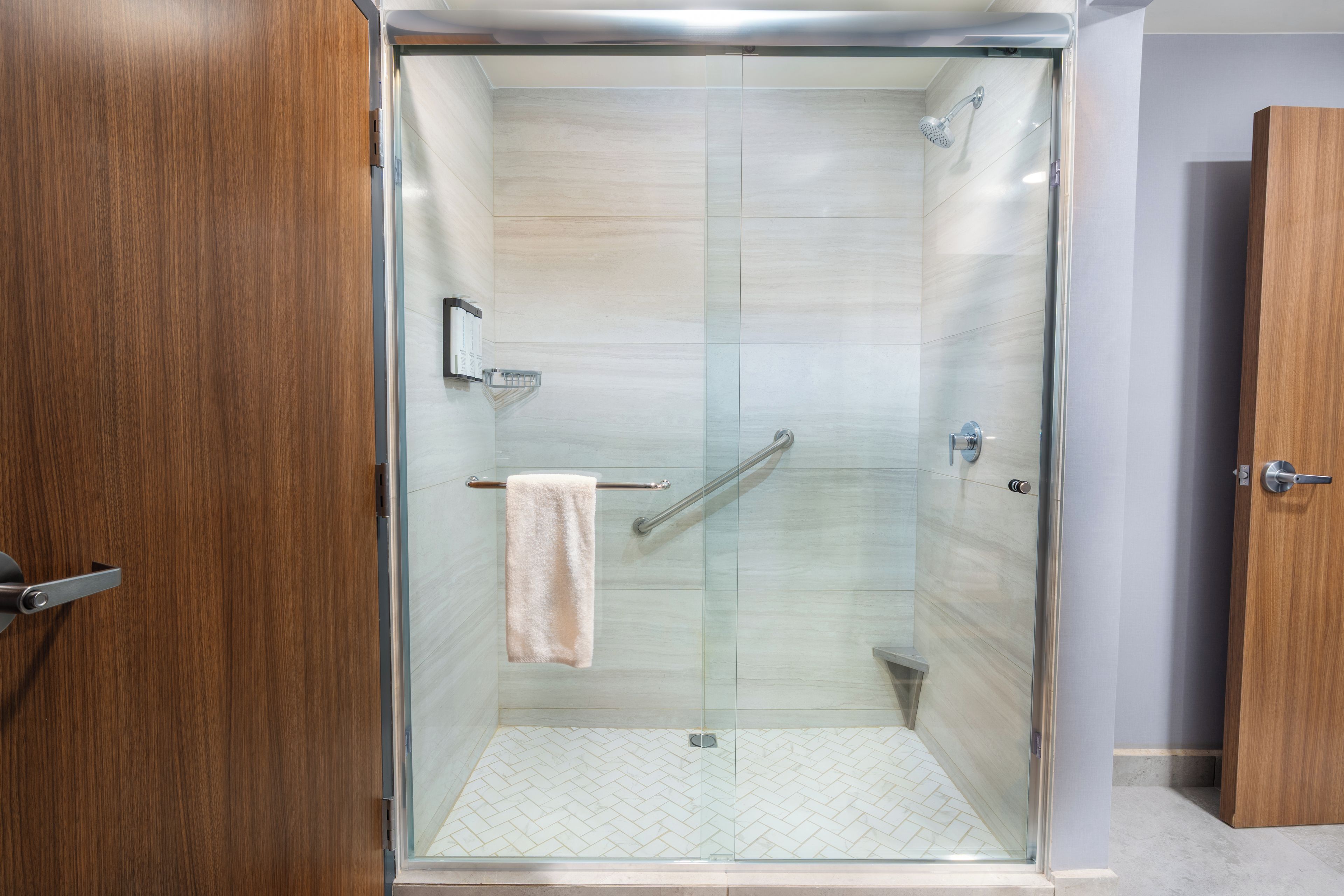 A glass-enclosed shower stall with a towel hanging on a rack, a handheld showerhead, and a glass door.