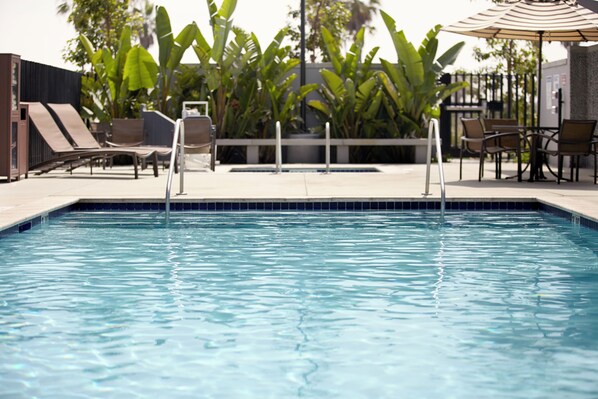 A swimming pool with lounge chairs and a table, surrounded by tropical plants. - Hyatt Place Piedras Negras (Piedras Negras)