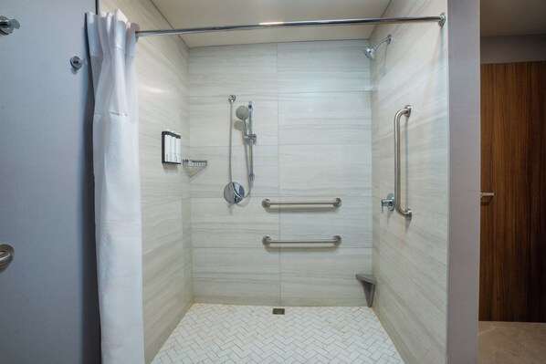 A walk-in shower with a glass door, a showerhead, a handheld shower, and a grab bar.