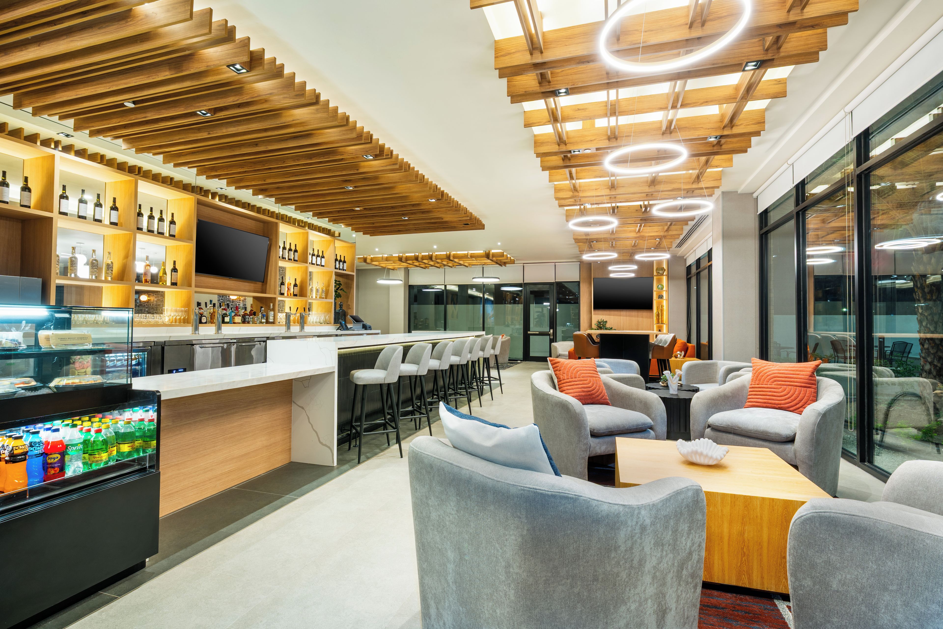 A modern bar area with a wooden ceiling, bar stools, and a variety of bottles.