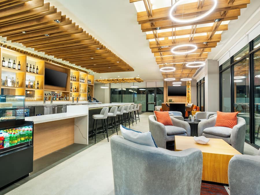 A modern bar area with a wooden ceiling, bar stools, and a variety of bottles.