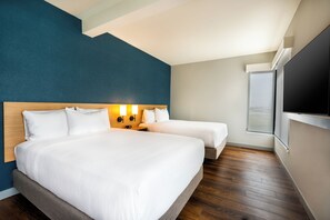 Habitación de hotel con una cama grande, dos mesitas de noche, un televisor y vistas al exterior.
