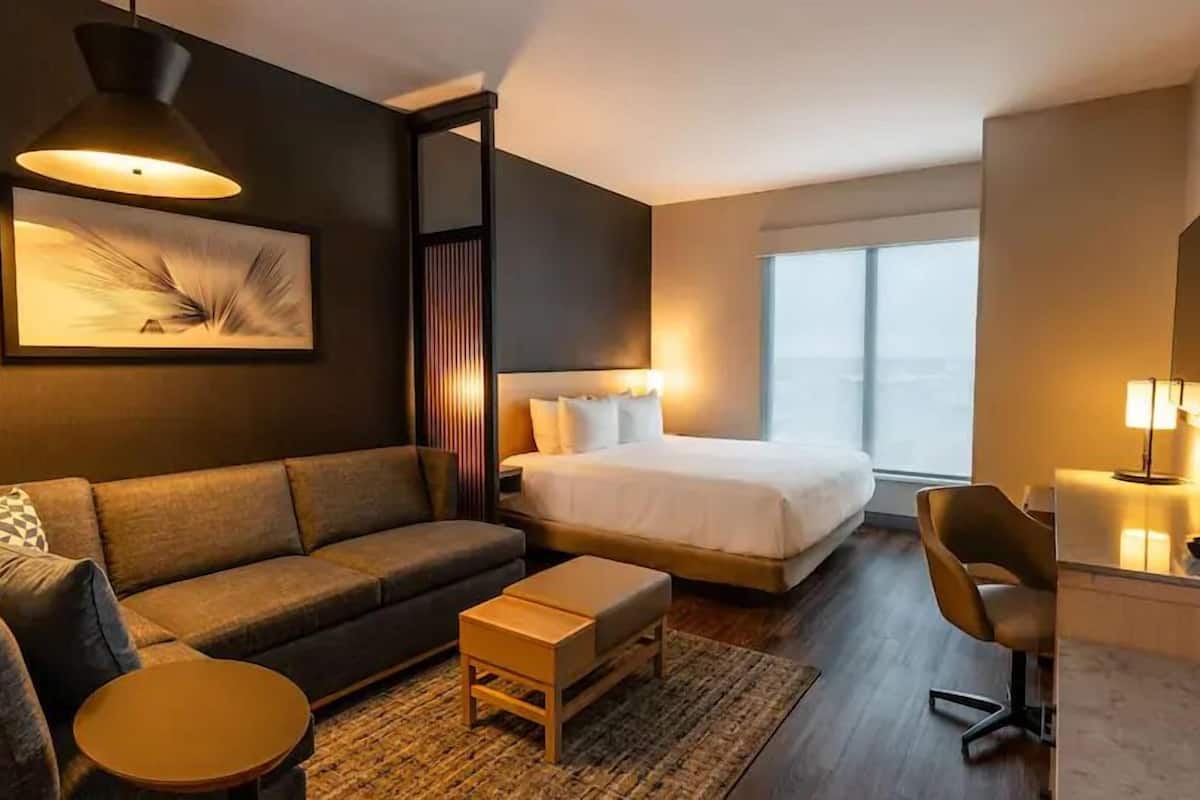 Una habitación de hotel moderna con una cama grande, un sofá, una mesita y un escritorio con una silla.