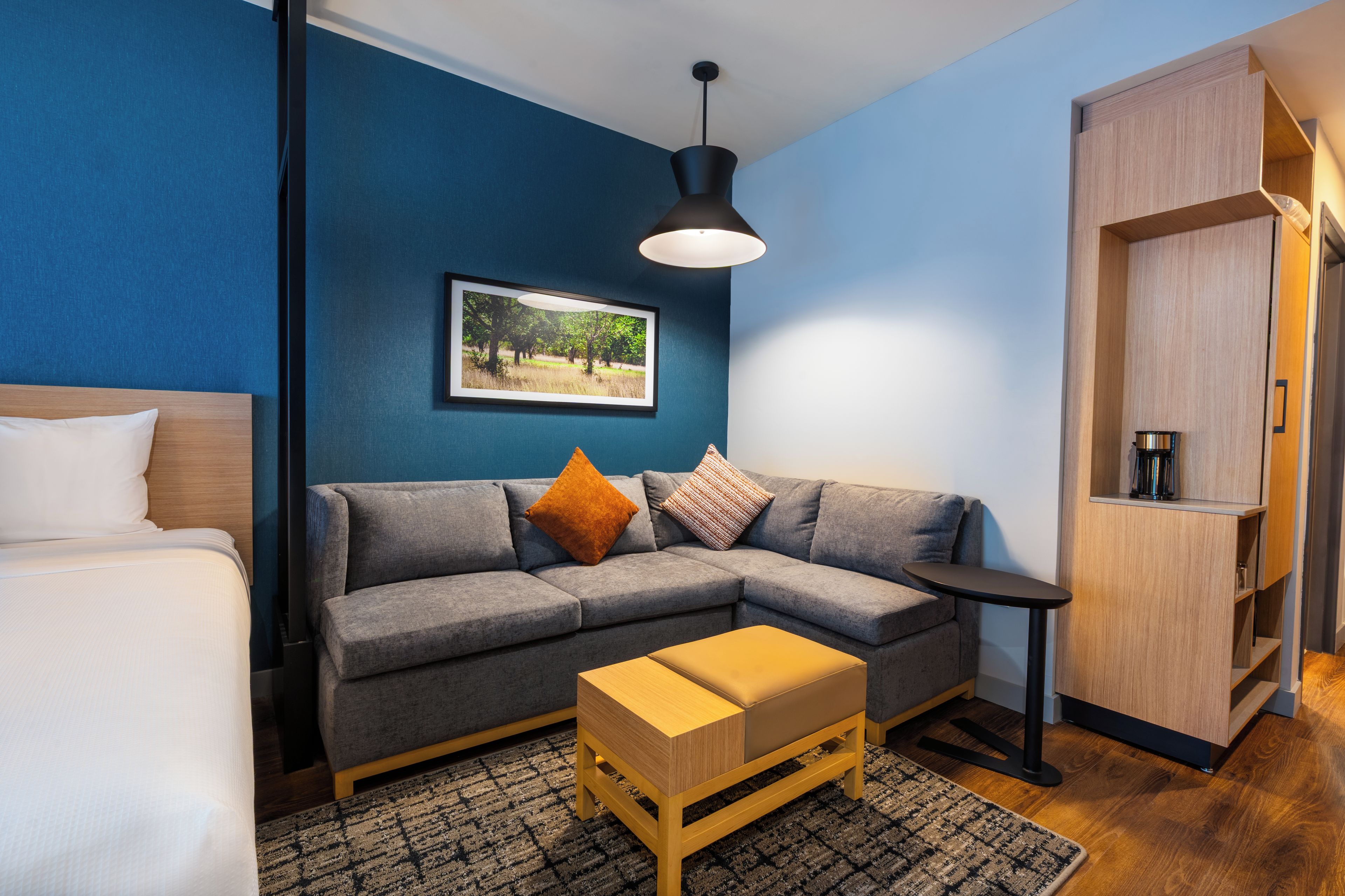 A modern room with a grey sofa, a wooden side table, a small wooden bench, a framed picture on the wall, and a wardrobe.