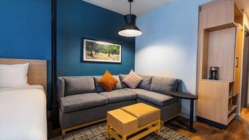 A modern room with a grey sofa, a wooden side table, a small wooden bench, a framed picture on the wall, and a wardrobe.