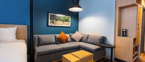 Una habitación moderna con un sofá gris, una mesita de madera, un pequeño banco de madera, un cuadro enmarcado en la pared y un armario.