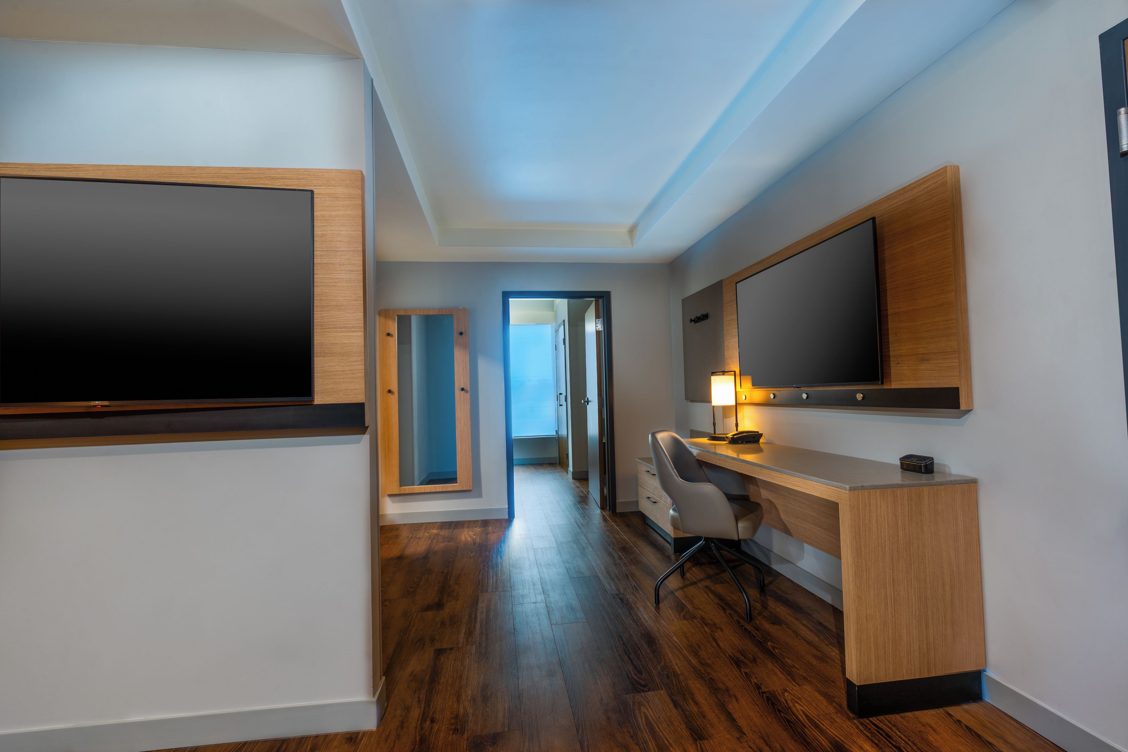 Une chambre d’hôtel moderne dotée d’un grand téléviseur à écran plat fixé au mur, d’un bureau en bois avec une chaise et d’un dressing.