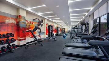 Un gimnasio con cintas de correr, máquinas de pesas y una pared con un mural colorido.