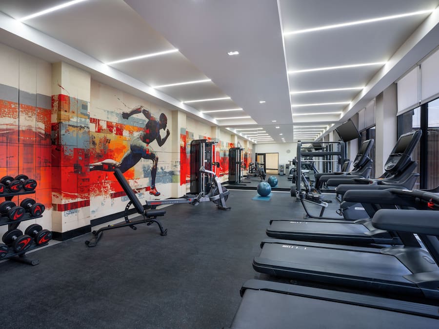 Un gimnasio con cintas de correr, máquinas de pesas y una pared con un mural colorido.