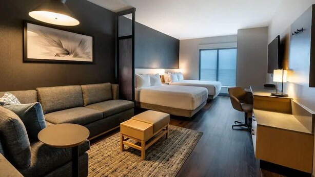 A modern hotel room with a grey sofa, two single beds, a small wooden table, and a desk with a chair. - Hyatt Place Piedras Negras (Piedras Negras)