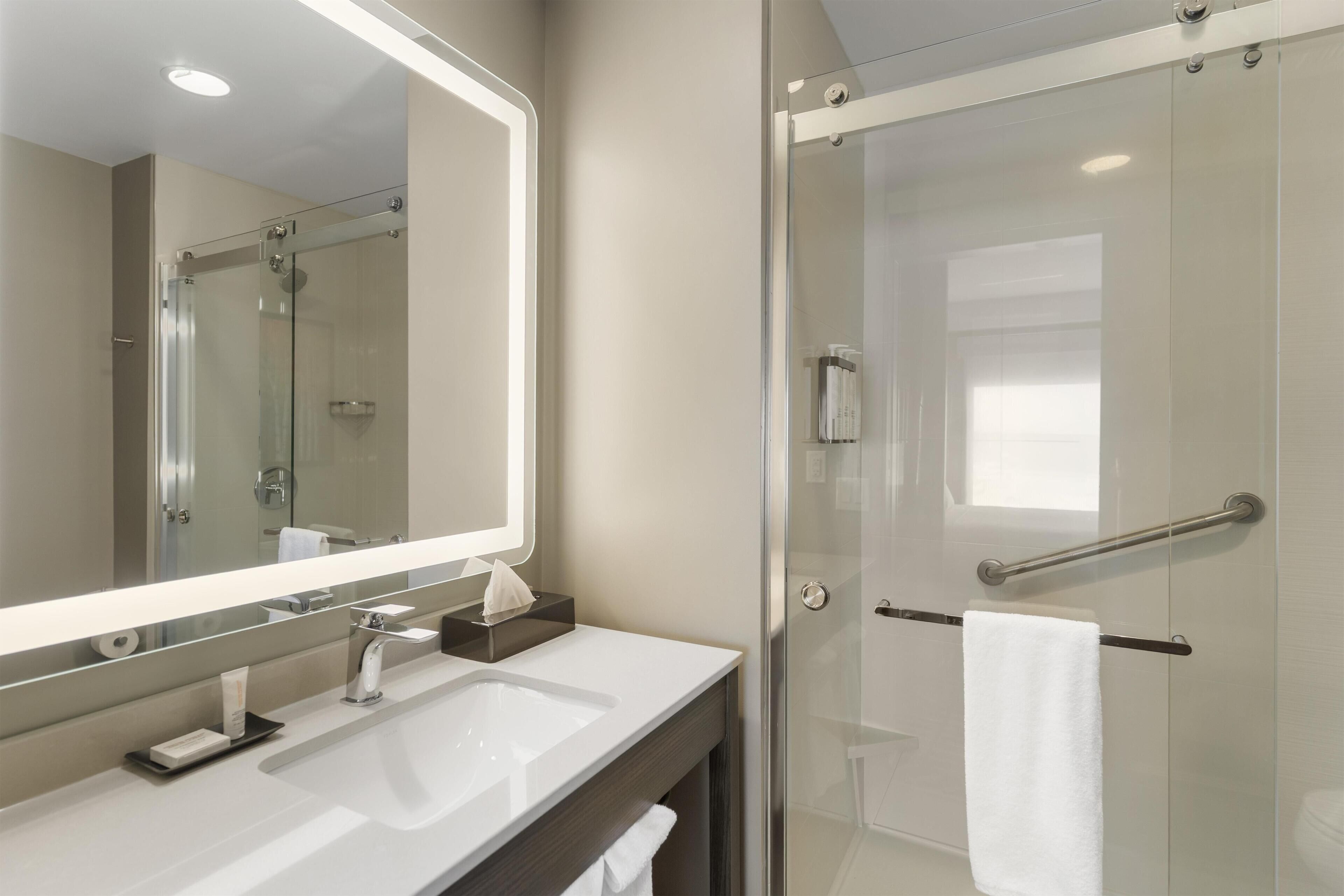 A modern bathroom with a large mirror, a sink, a glass shower enclosure, and a towel rack.